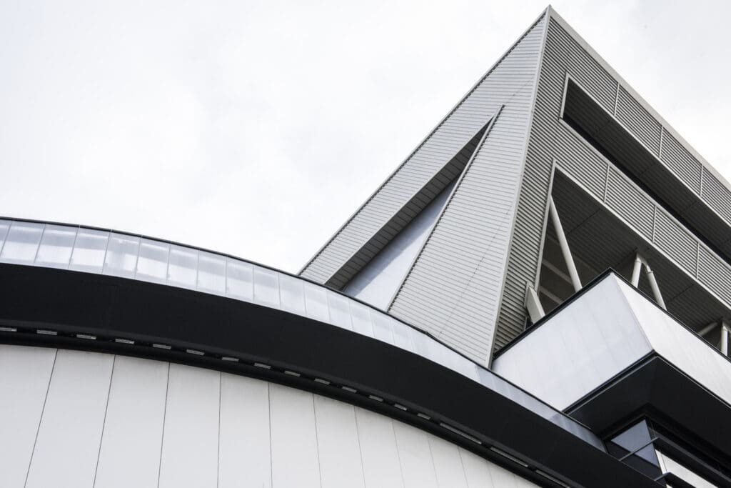 A modern building with sharp angles and geometric lines, featuring a mix of metal and glass materials, set against a cloudy sky. The architectural design emphasizes clean, intersecting shapes.