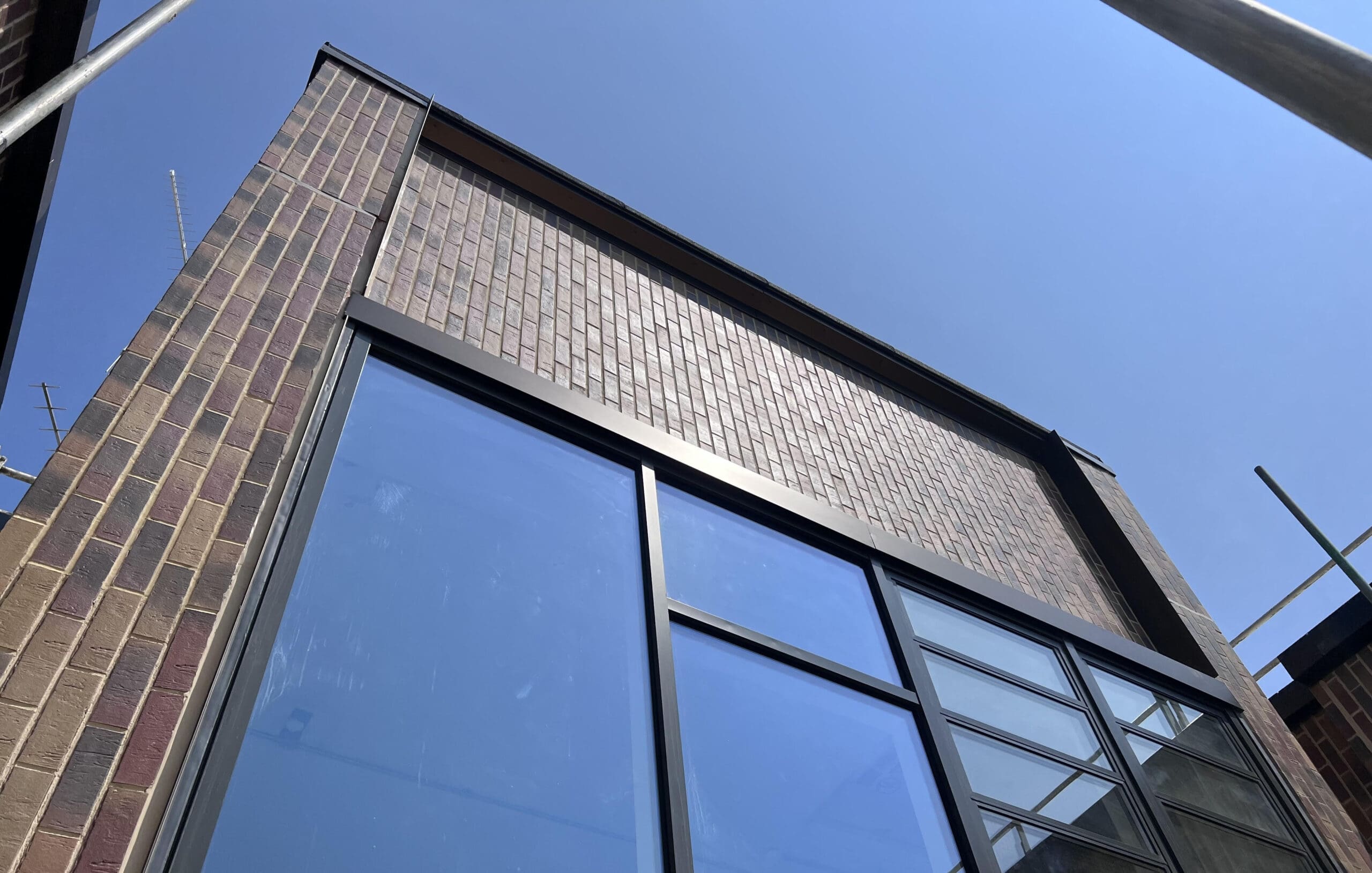 A low-angle view of a modern brick building with large blue-tinted glass windows, set against a clear blue sky.